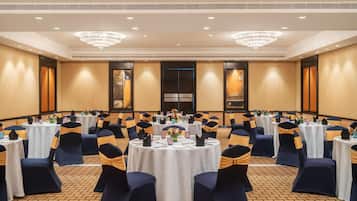 A conference room with round tables, navy blue chairs with gold sashes, and chandeliers.