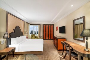 Una camera d'albergo con un letto grande, una scrivania, una sedia, una TV e una finestra con vista sulla città.