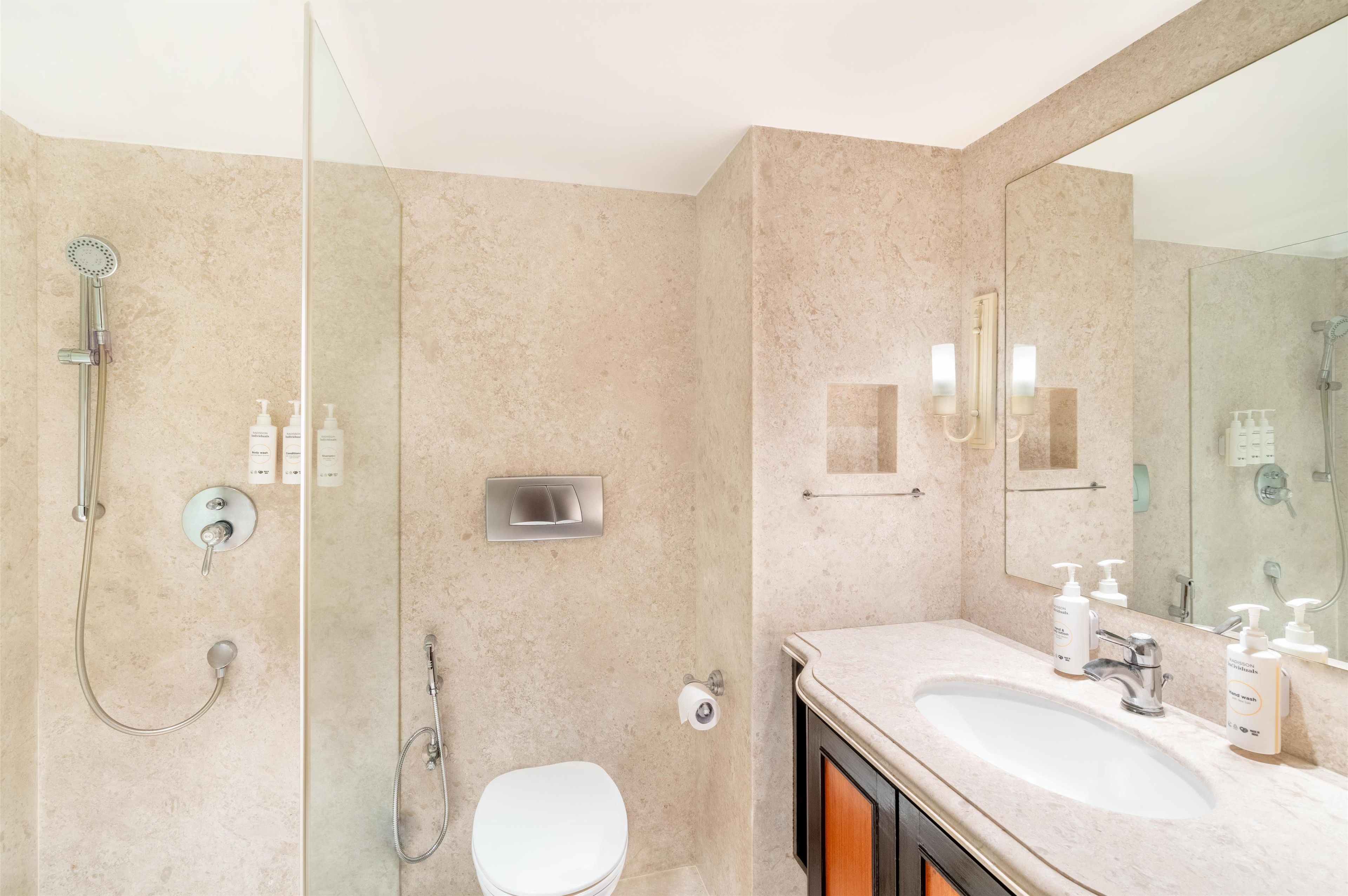 A modern bathroom with a glass-enclosed shower, a white toilet, and a vanity with a large mirror and sink.