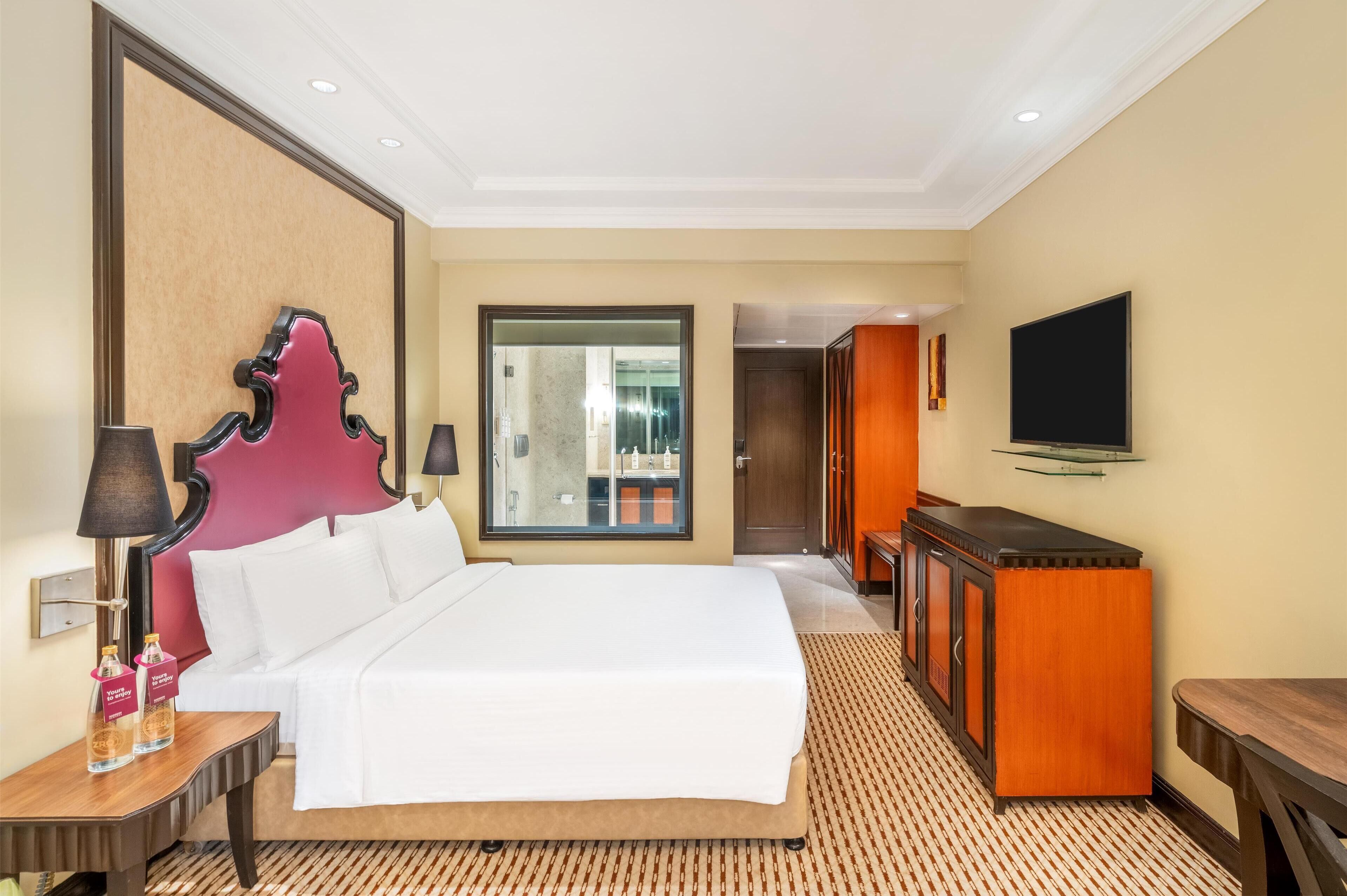 A hotel room with a large bed, a wooden desk, a television, and a mirror.