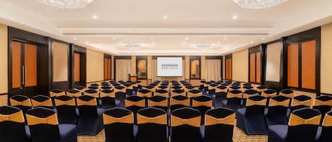 Un salón de conferencias con filas de sillas, una pantalla grande y candelabros.