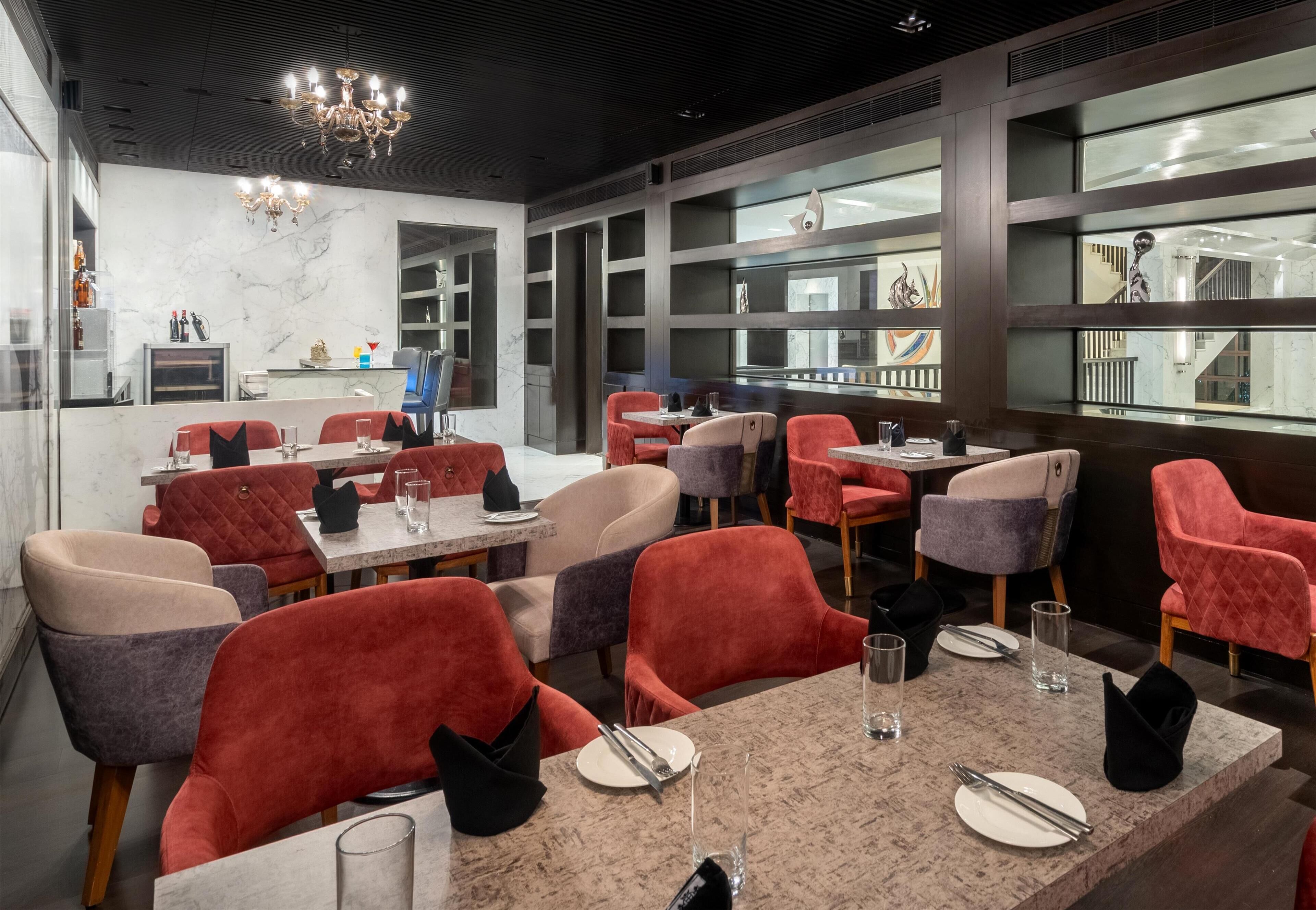 A modern restaurant with red and grey upholstered chairs, marble tables, and a chandelier.
