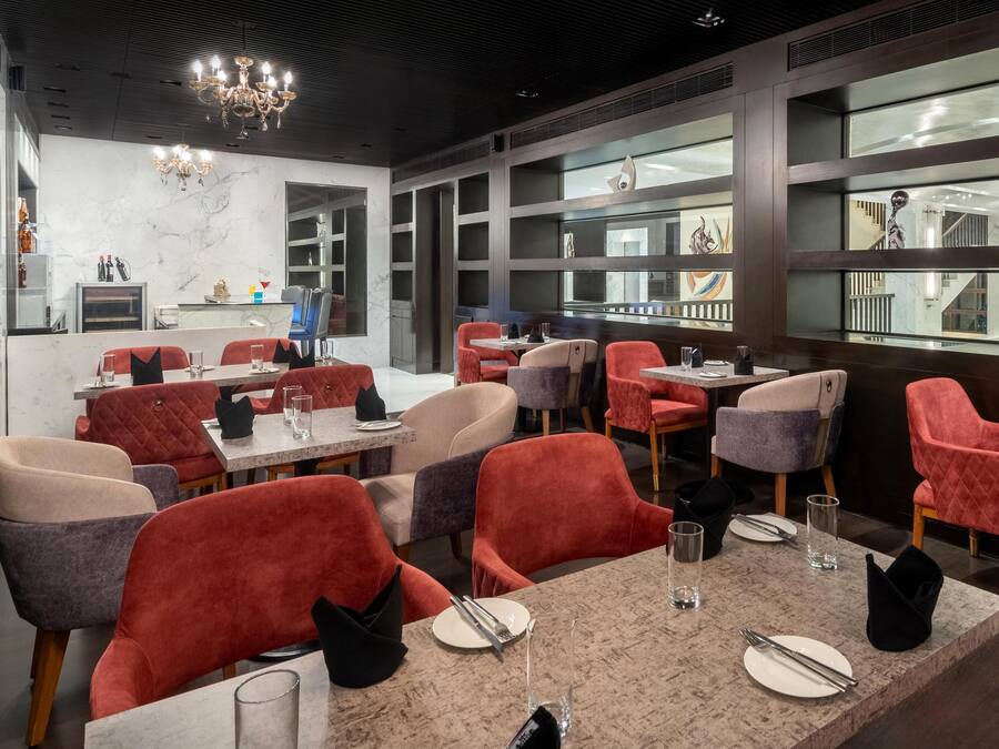 A modern restaurant with red and grey upholstered chairs, marble tables, and a chandelier.