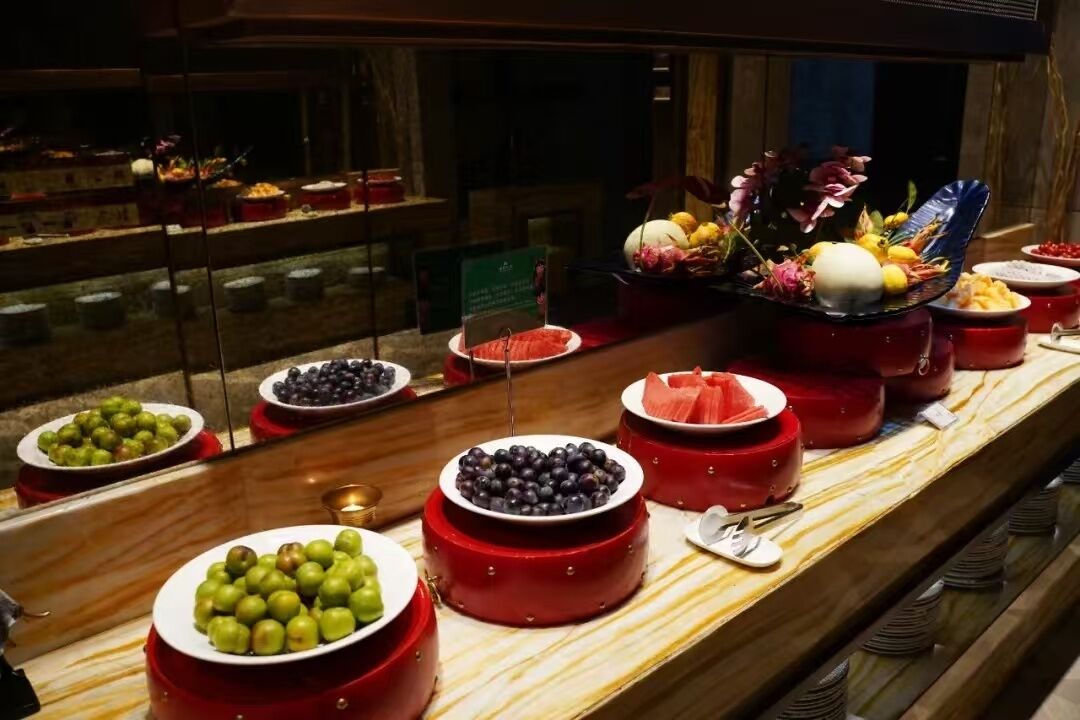 A buffet with various fruits and vegetables displayed in red bowls.