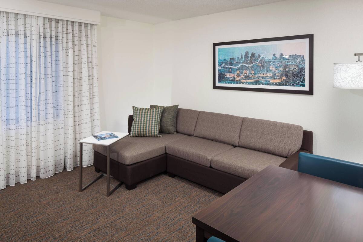 A modern living room with a sectional sofa, a small side table, a framed cityscape picture, and a lamp.