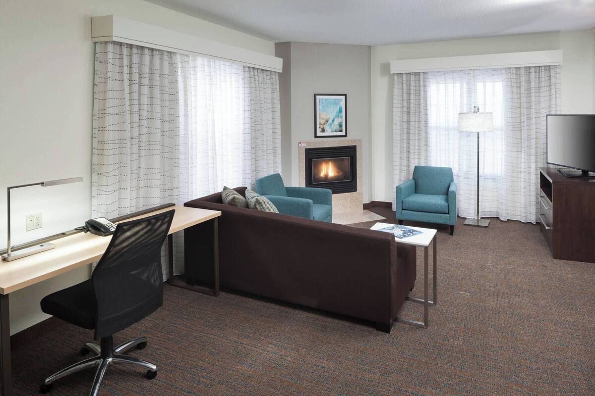 A hotel room with a sofa, armchair, desk, and a fireplace.