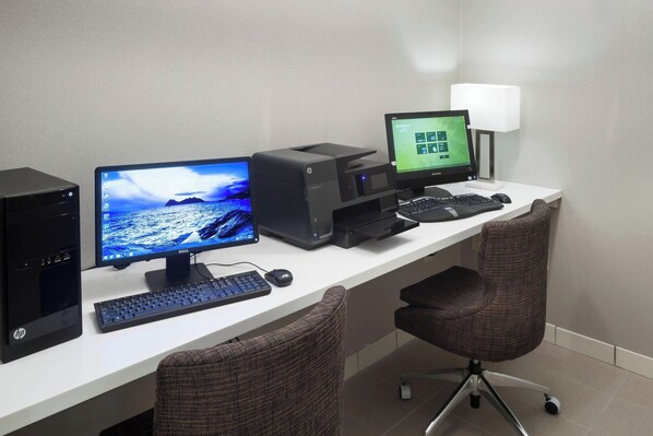 Un espacio de trabajo con dos monitores, un ordenador de escritorio, una impresora y una lámpara.