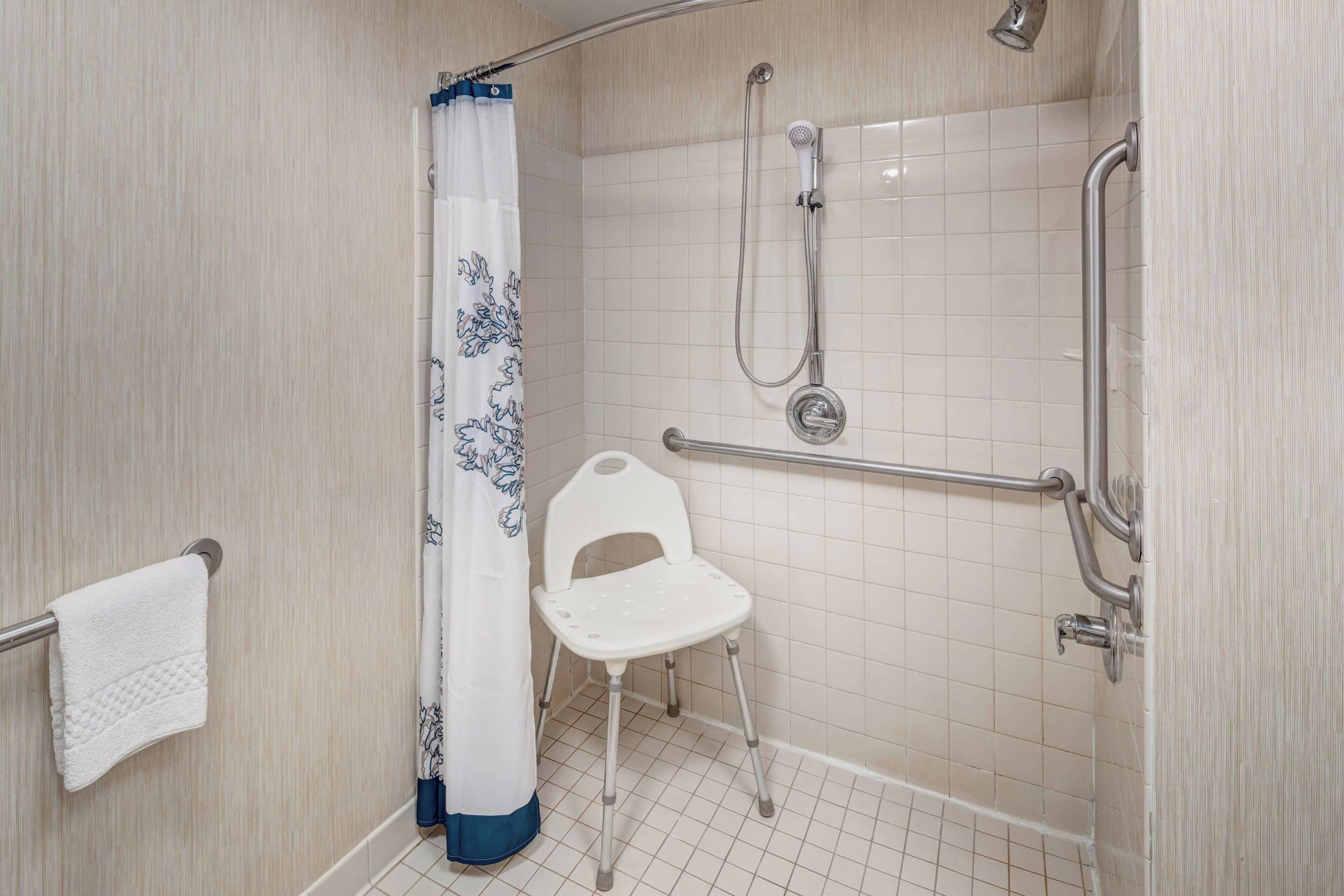 A shower area with a white chair, a showerhead, and a grab bar.