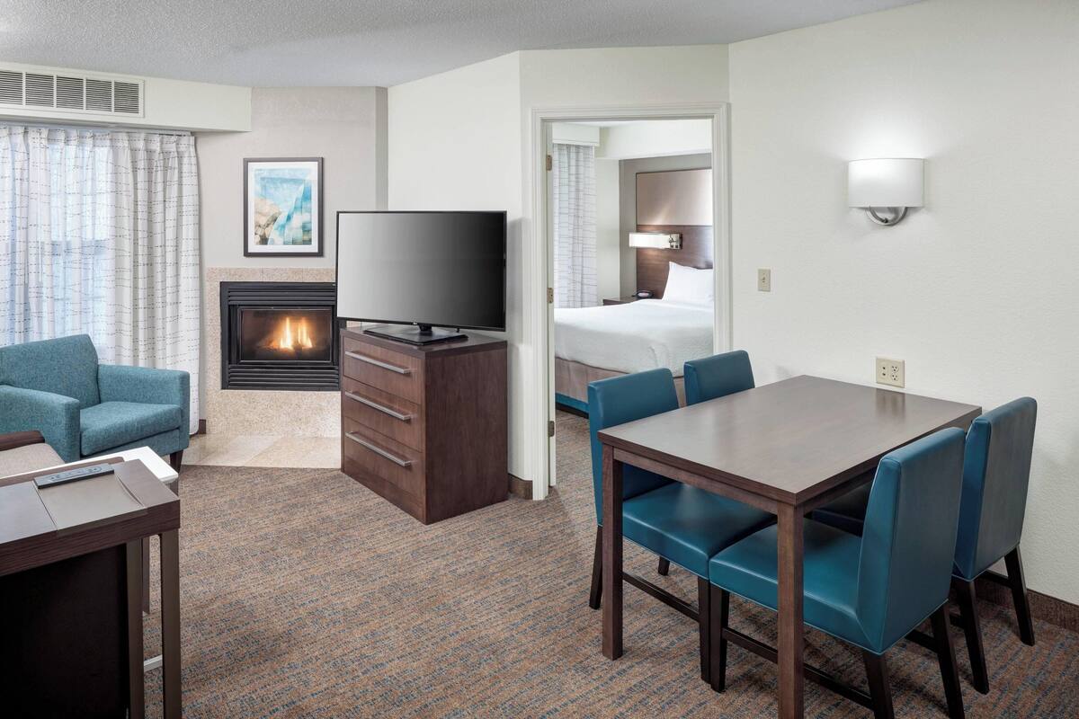 A hotel room with a TV, fireplace, dining area, and a bed.