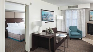 A hotel room with a bed, a desk with a lamp, a chair, and a framed cityscape picture on the wall. - Residence Inn by Marriott Kansas City Country Club Plaza (Kansas City)