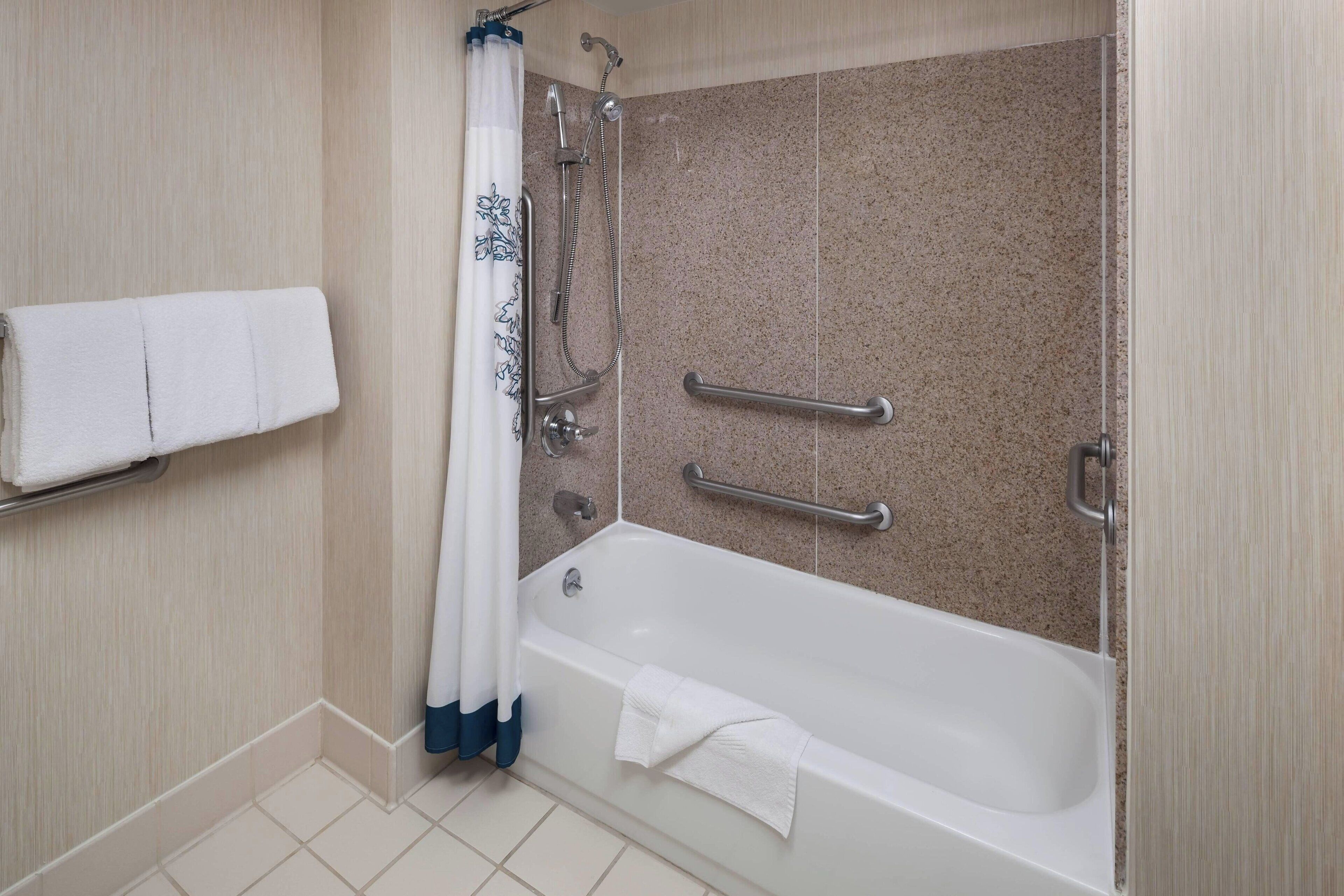A bathroom with a bathtub, a shower, and a handrail.