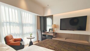 A hotel room with a large bed, a desk with a lamp, a chair, a TV, and a window with curtains. - Merry Hotel Shanghai (Shanghai)