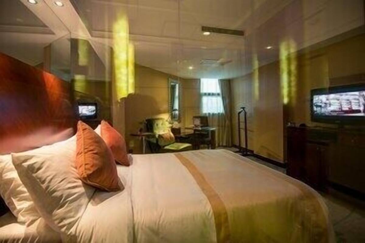A hotel room with a bed, pillows, a desk, a chair, a television, and a window.