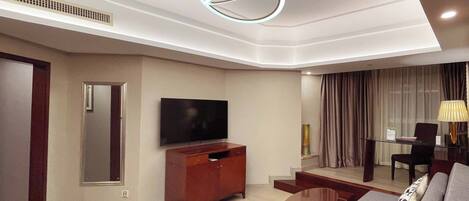 A modern living room with a flat-screen TV, wooden furniture, a glass coffee table, and a unique circular ceiling light.