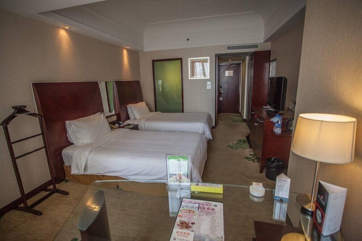 A hotel room with two beds, a desk with a chair, a TV, and a lamp.