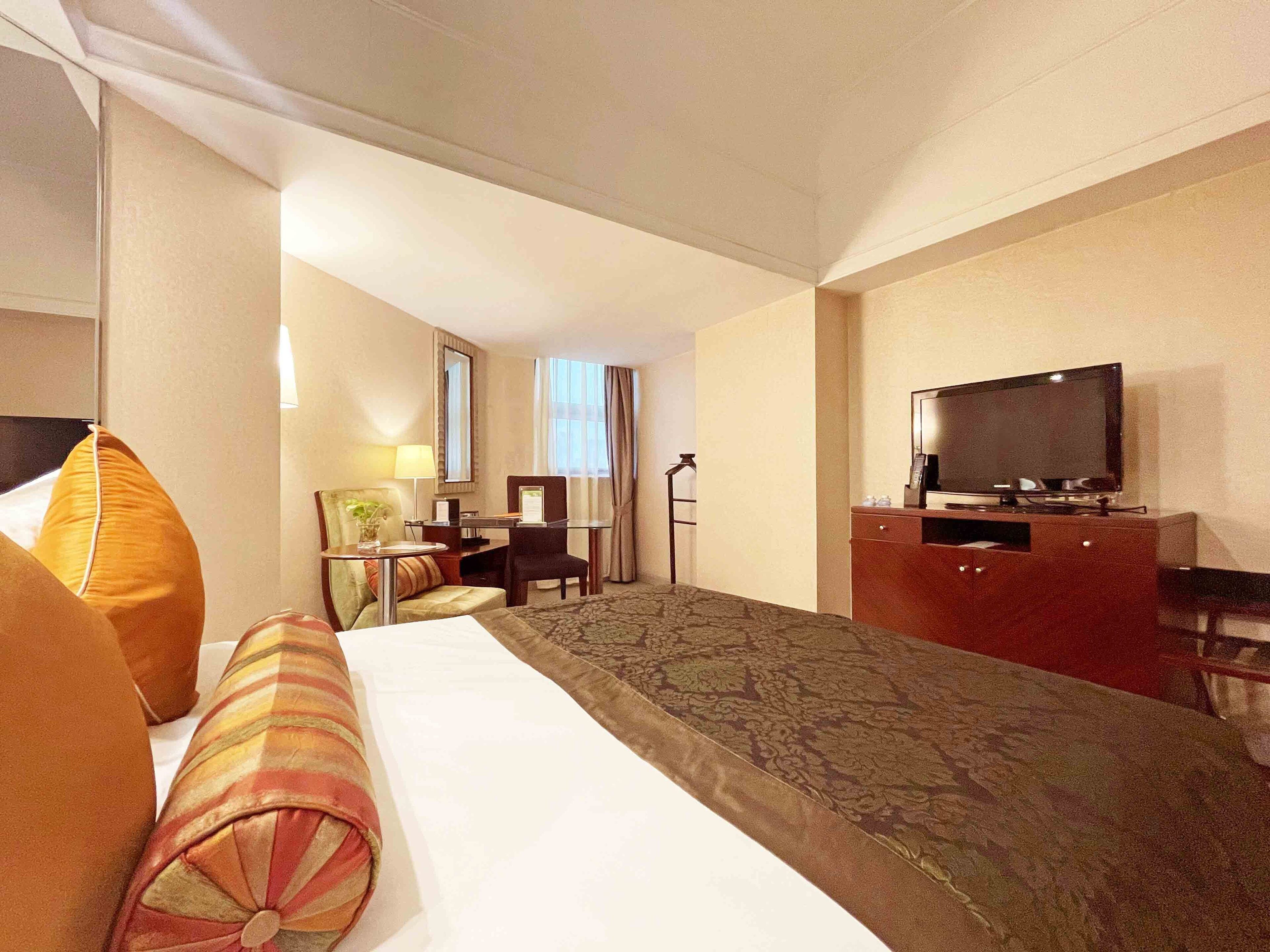 Una habitación de hotel con cama, escritorio, silla, televisor y ventana con cortinas.
