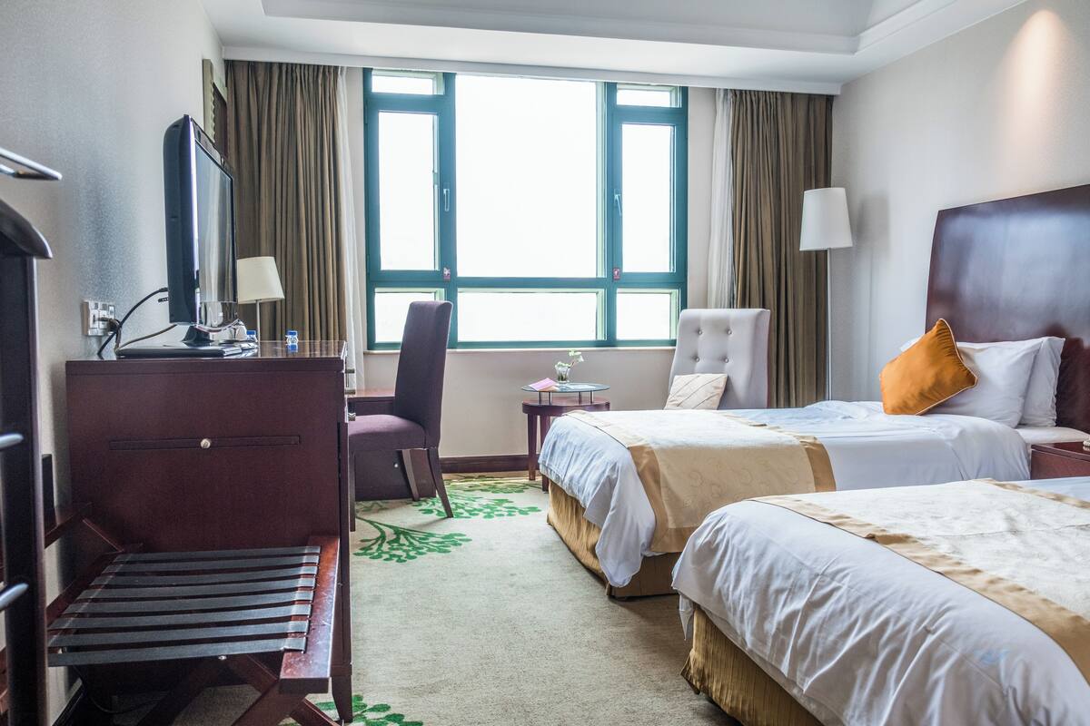 A hotel room with two beds, a desk, a chair, a TV, and a window with curtains.