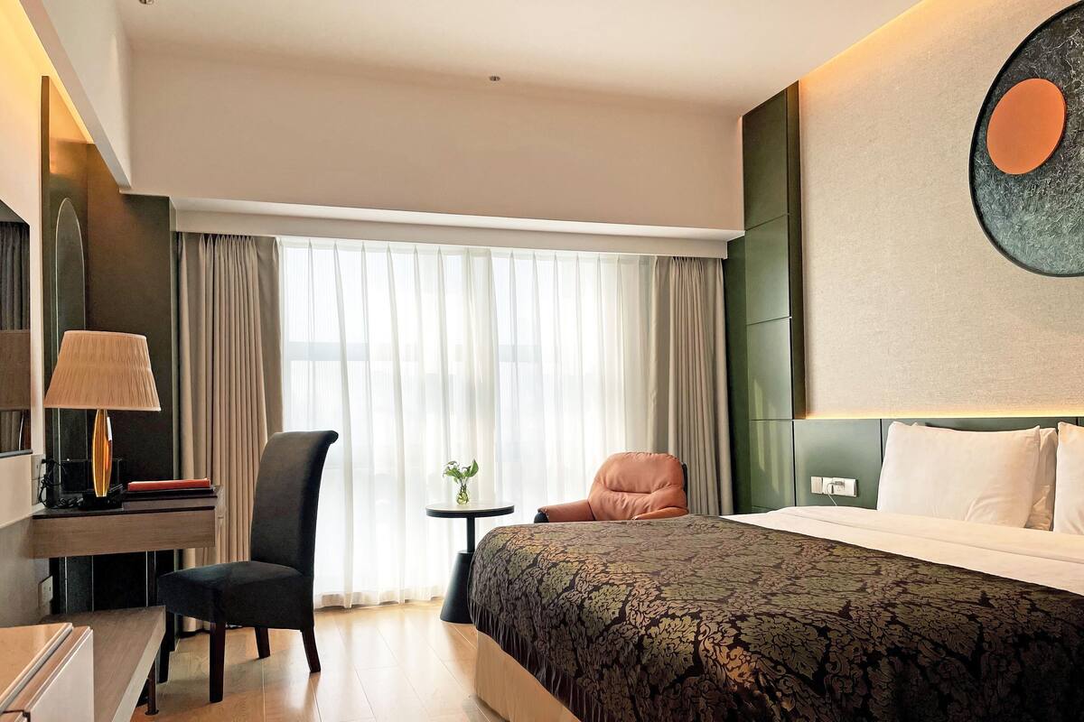 A hotel room with a bed, a desk, a chair, and a small table with a plant.