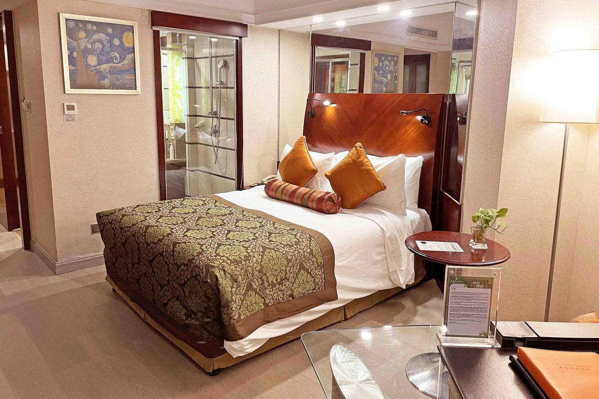 A hotel room with a large bed, a bedside table, a mirror, and a shower area.