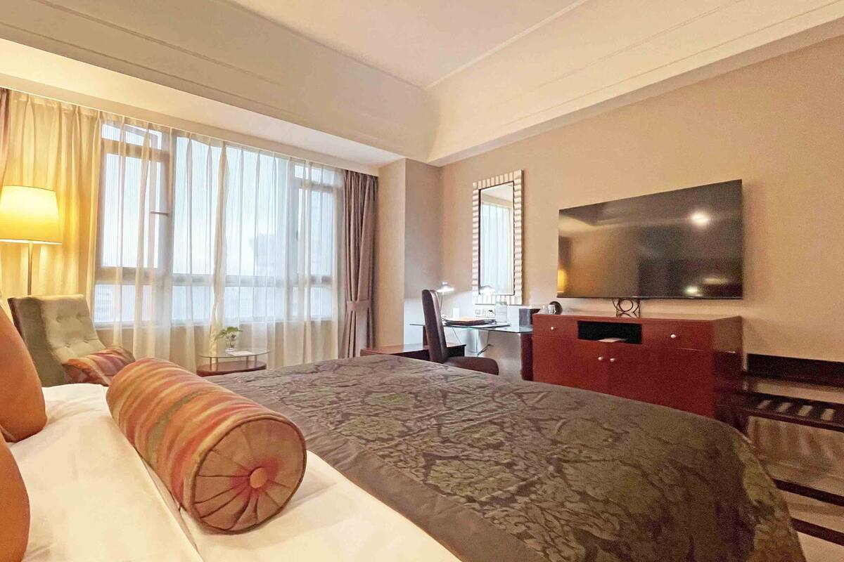 A hotel room with a bed, a desk, a chair, a television, and a window with curtains.