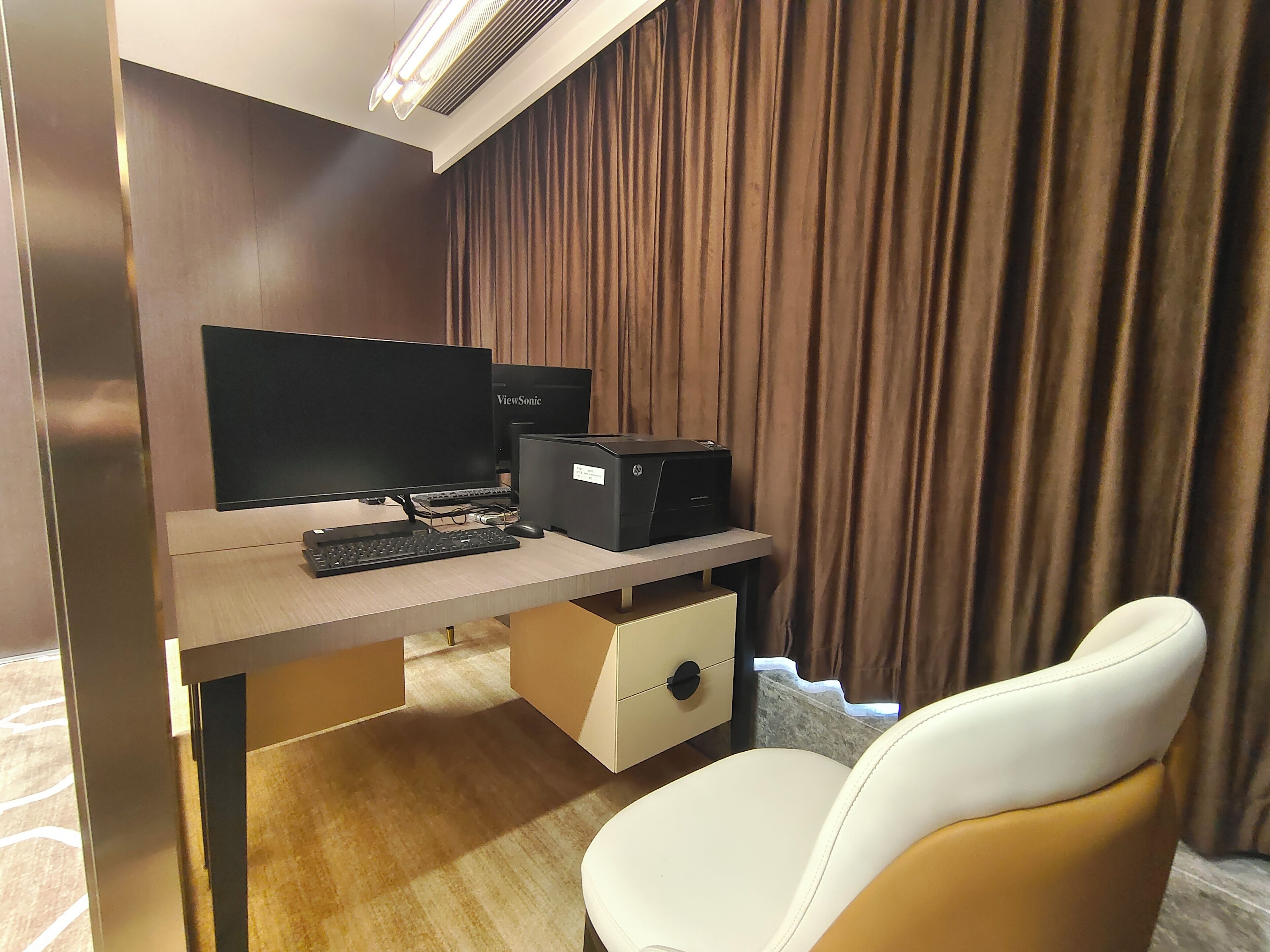 A modern office space with a desk, computer, printer, and a white chair.