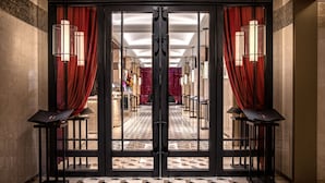 Un vestíbulo de hotel con piso a cuadros, cortinas rojas y dos lámparas de pie altas.