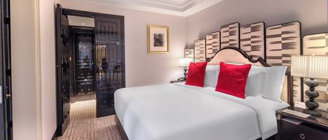 A hotel room with a large bed, a nightstand, a lamp, a framed picture on the wall, and a door leading to another room.