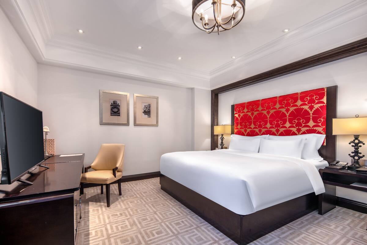 A hotel room with a large bed, a desk, a chair, a television, and framed pictures on the wall.