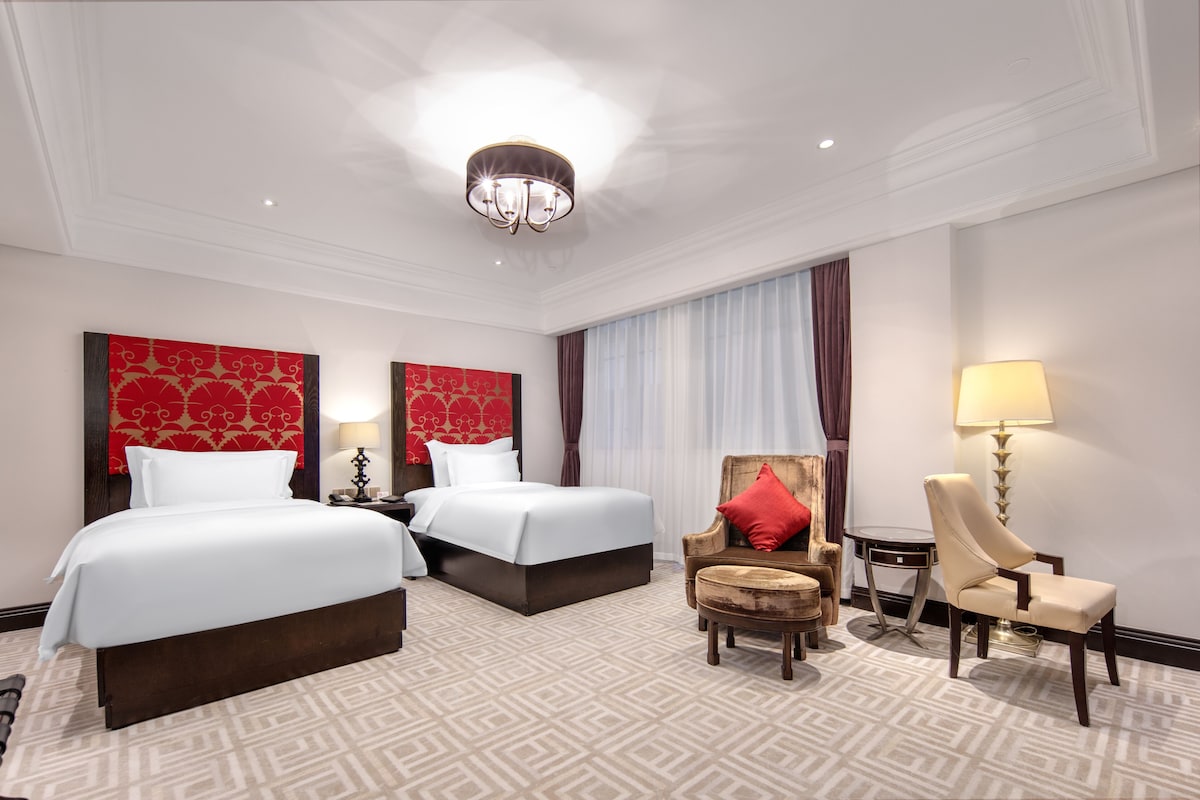 A hotel room with two beds, a sofa, a chair, and a lamp.
