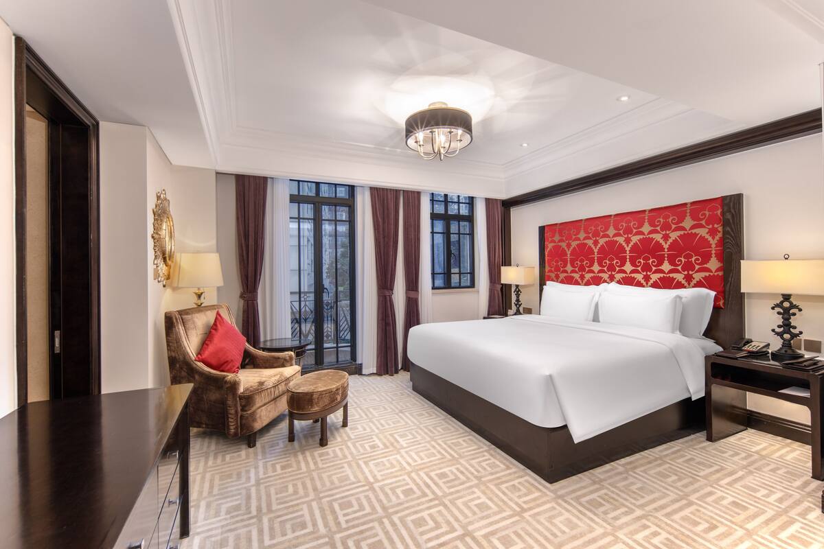 A hotel room with a large bed, a chair, a small table, and a nightstand.
