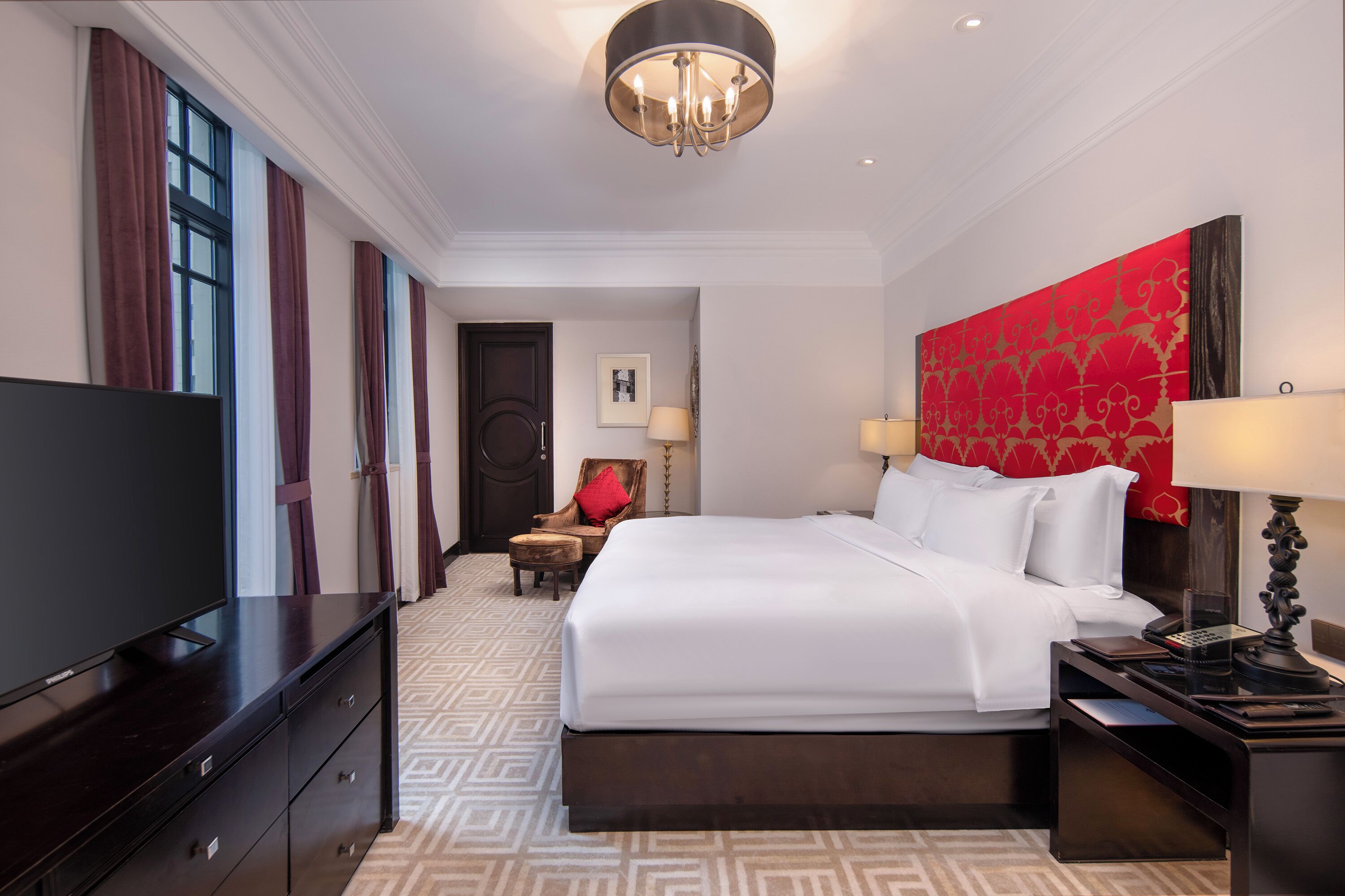 A hotel room with a large bed, a TV, a desk with a phone, and a chair.