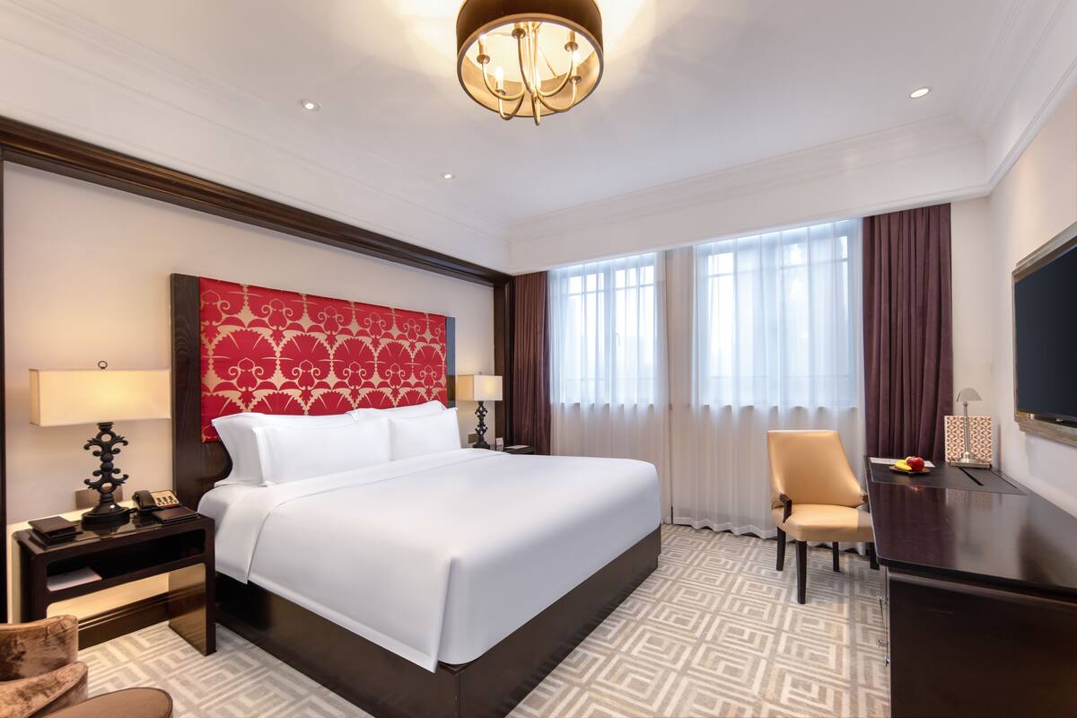 A hotel room with a large bed, a desk, a chair, and a television.