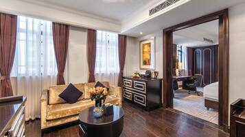 Quarto de hotel com um sofá dourado, uma mesa de centro preta, uma escrivaninha com cadeira, uma cama e um banheiro visível por uma porta aberta.