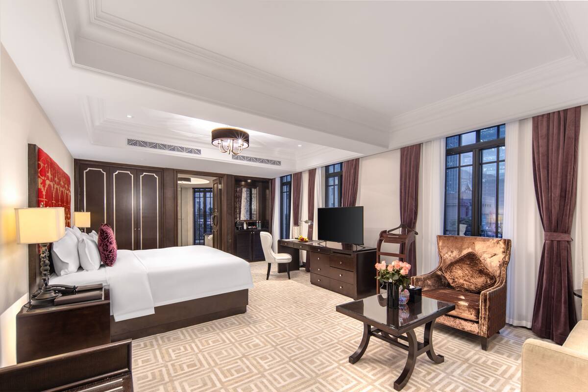 A hotel room with a large bed, a desk, a TV, and a chair.