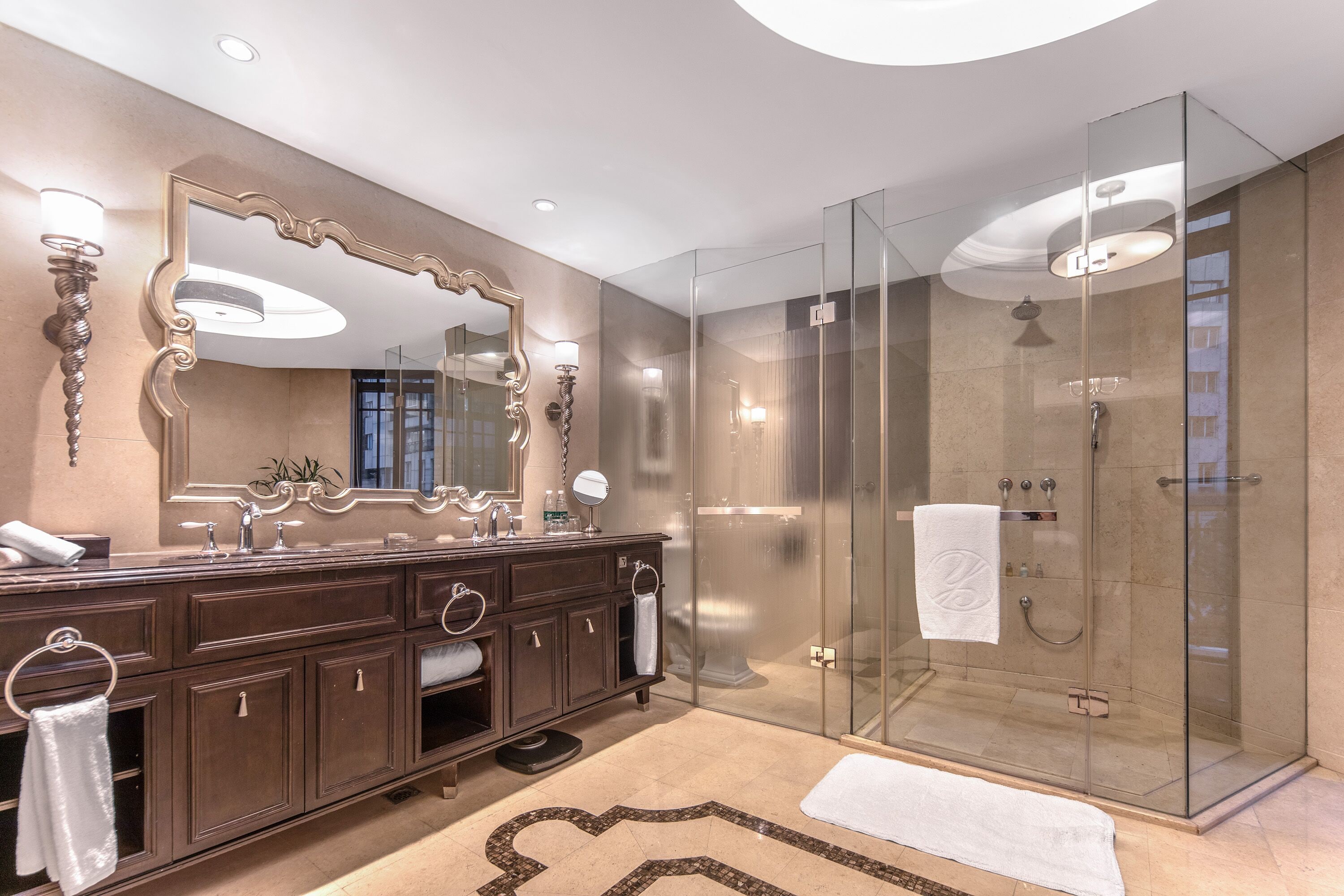 Un baño moderno con un espejo grande, tocador de madera oscura y ducha con mampara de vidrio.