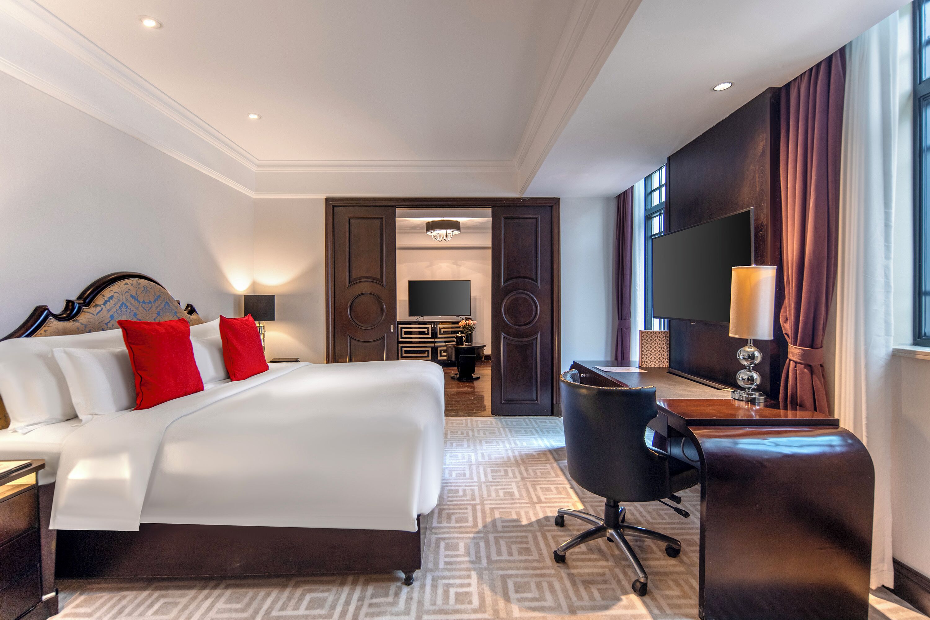 A hotel room with a large bed, a desk, a chair, a TV, and a wardrobe.
