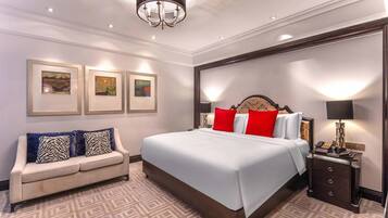 Una habitación de hotel con una cama grande, un sofá, una mesita de noche y cuadros en las paredes.