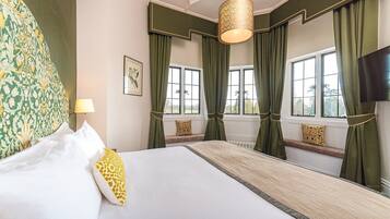 A hotel room with a large bed, green curtains, a hanging lamp, and a view of the outdoors through the windows.