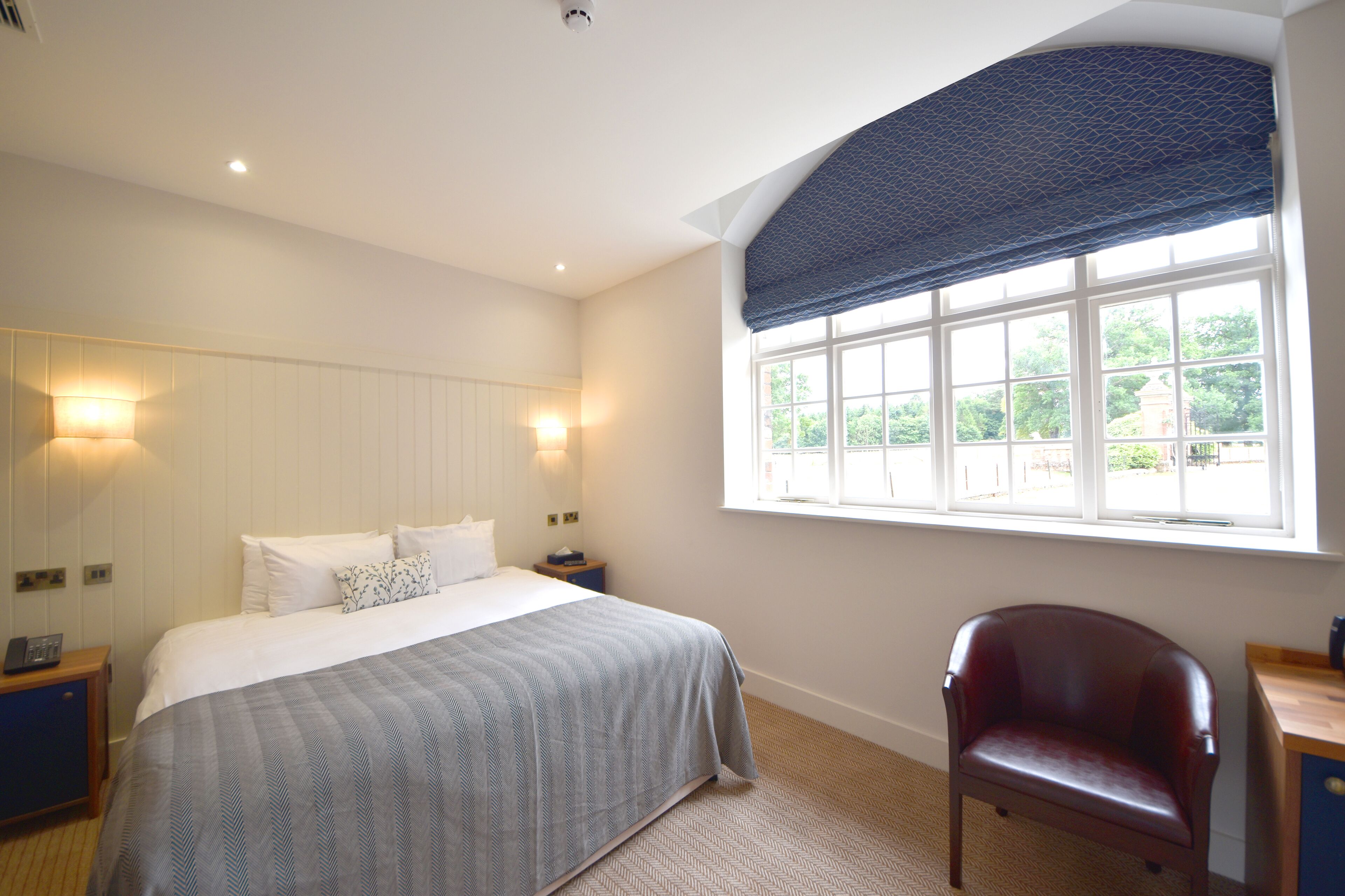 A bedroom with a large bed, bedside lamps, a window with a blue valance, and a wooden chair.