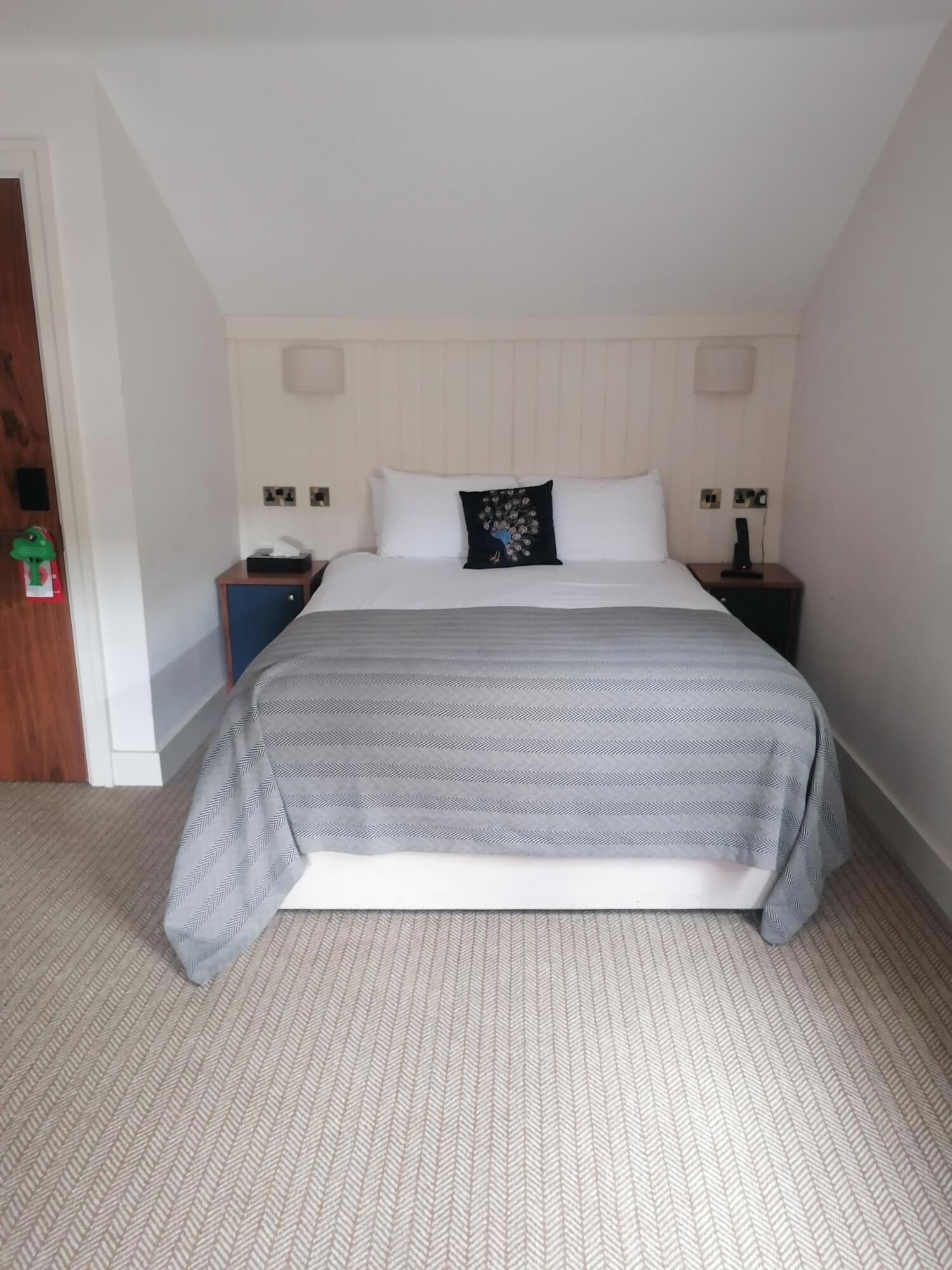 A bedroom with a bed, two bedside tables, a nightstand, a door, and a wall-mounted light fixture.