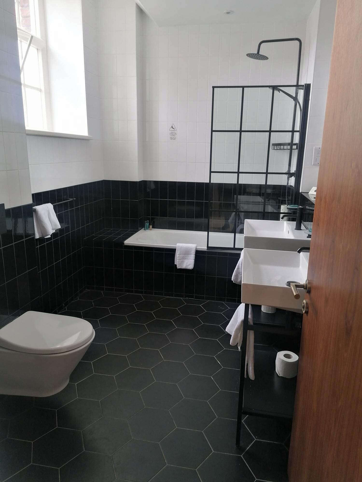 A modern bathroom with a black and white tiled design, a toilet, a shower, and a sink with a mirror.