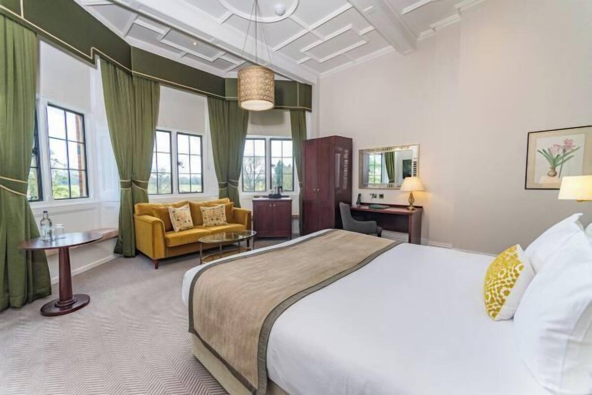 Une chambre d’hôtel avec un grand lit, un bureau, une chaise, un canapé et une fenêtre avec des rideaux.
