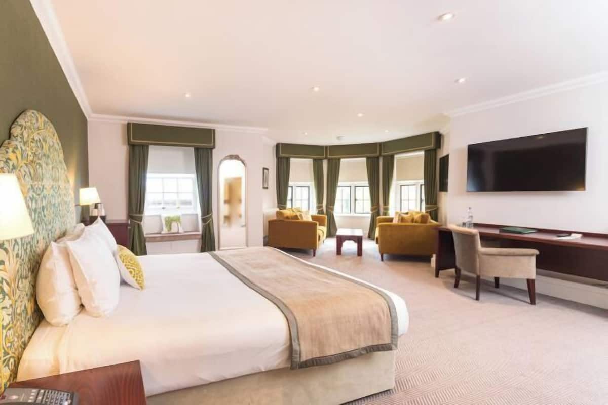 Une chambre d’hôtel avec un grand lit, un bureau, une télévision et deux fauteuils.