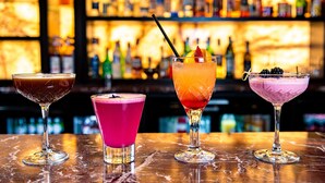 Tres cócteles sobre una barra, con un fondo borroso de estantes llenos de botellas.