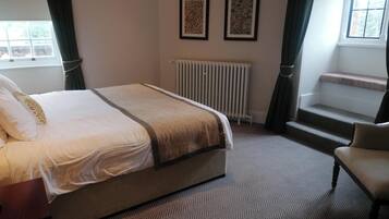 A hotel room with a bed, a chair, a radiator, and two framed pictures on the wall.