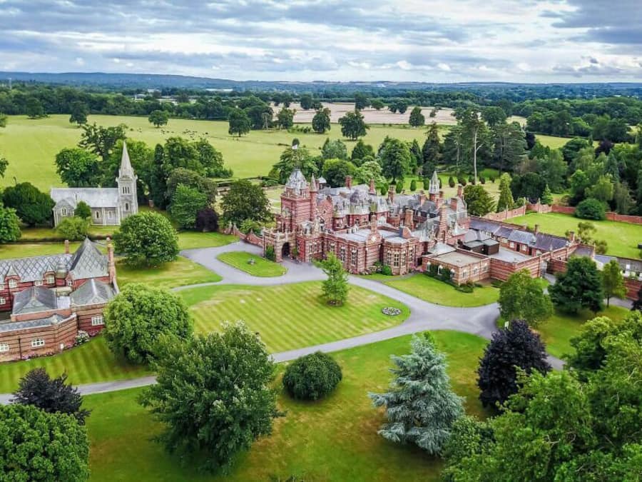 A large, historic estate with expansive green lawns, a prominent church, and a grand manor house.