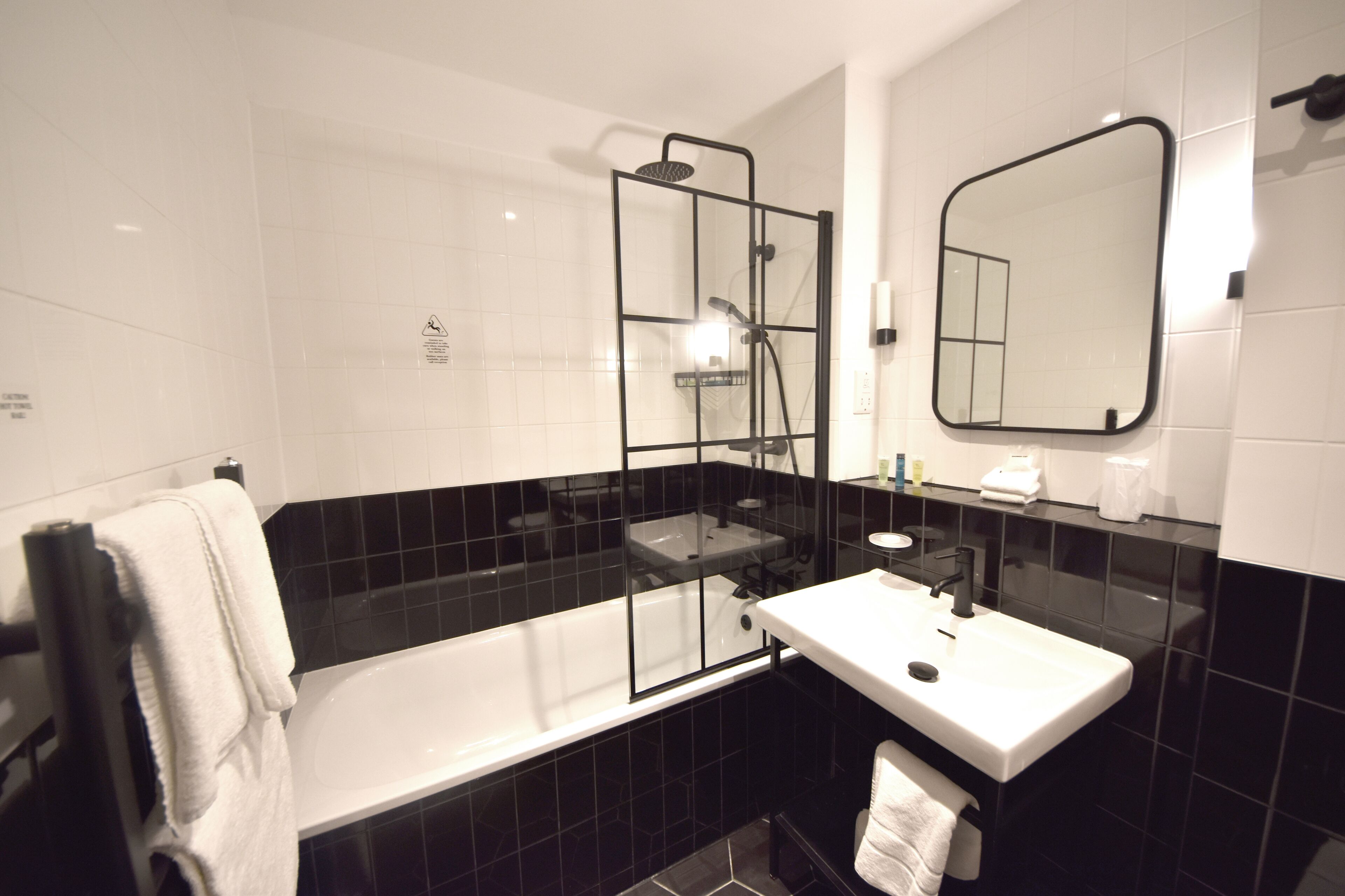 Un baño moderno con ducha envuelta en vidrio, lavamanos blanco y espejo grande.