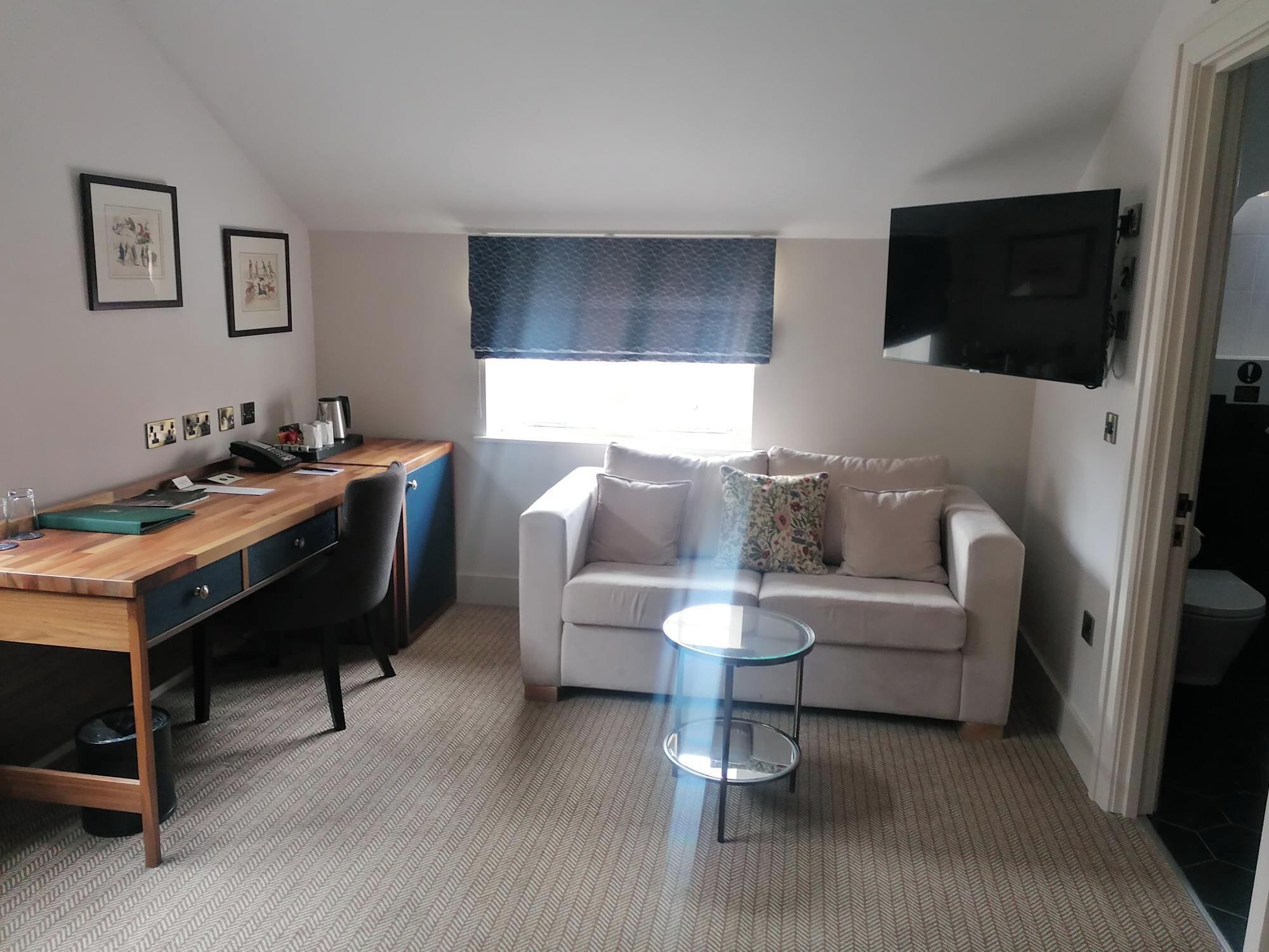 A compact living space with a wooden desk, a white sofa, a glass coffee table, and a TV mounted on the wall.