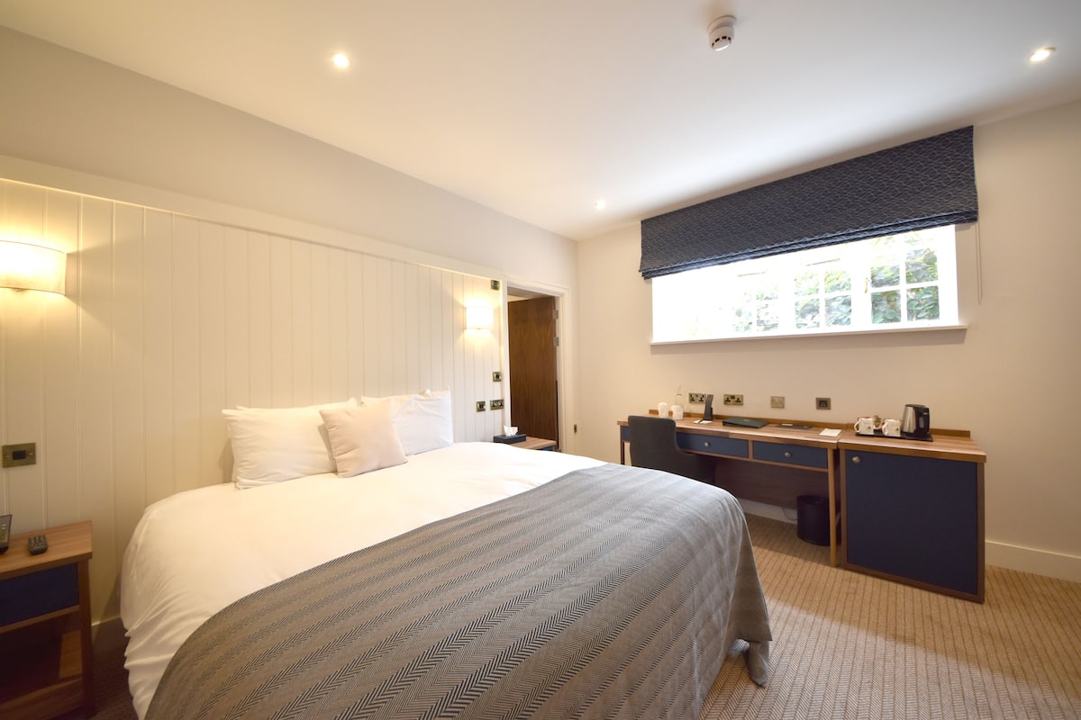 Une chambre d’hôtel avec un grand lit, un bureau et une fenêtre avec des stores.