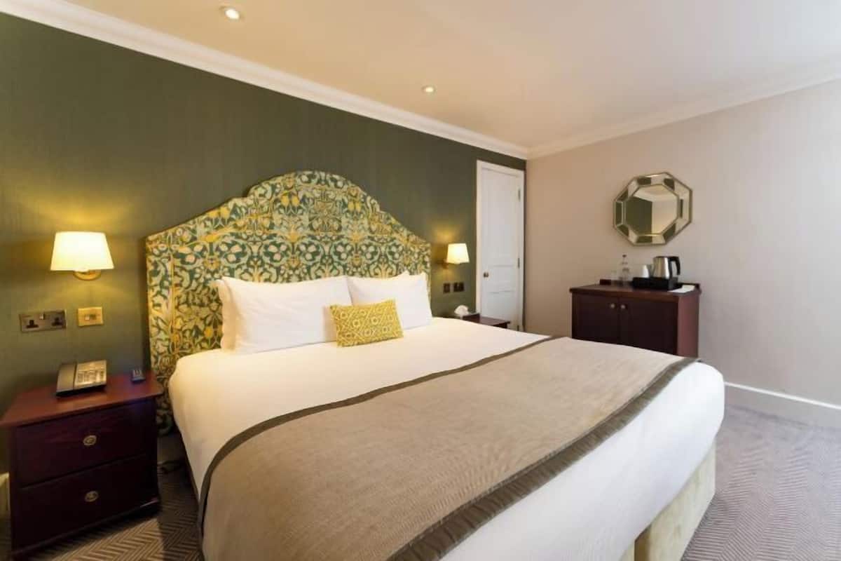 Une chambre d’hôtel avec un grand lit, deux lampes de chevet, une table de chevet, une commode et un miroir au mur.